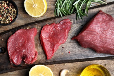 Photo of Fresh raw meat steaks and spices on wooden table, flat lay