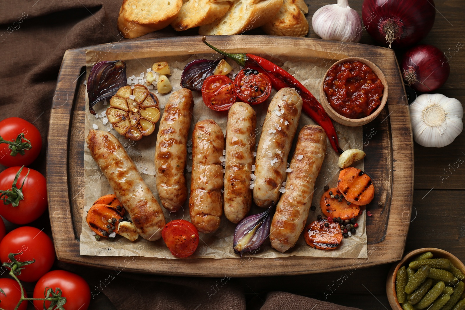 Photo of Tasty grilled sausages and products on wooden table, flat lay