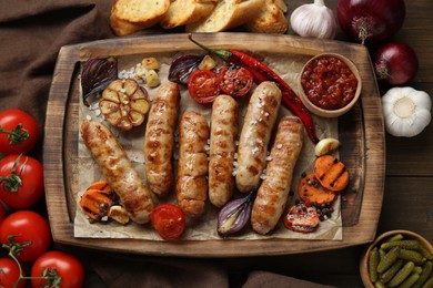 Tasty grilled sausages and products on wooden table, flat lay