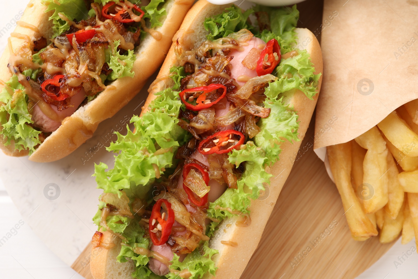 Photo of Tasty hot dogs with chili, lettuce, sauce and French fries on white table, top view