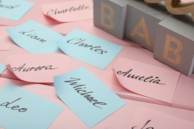 Cubes with word Baby and paper stickers with different names on pink wooden table. Choosing baby's name