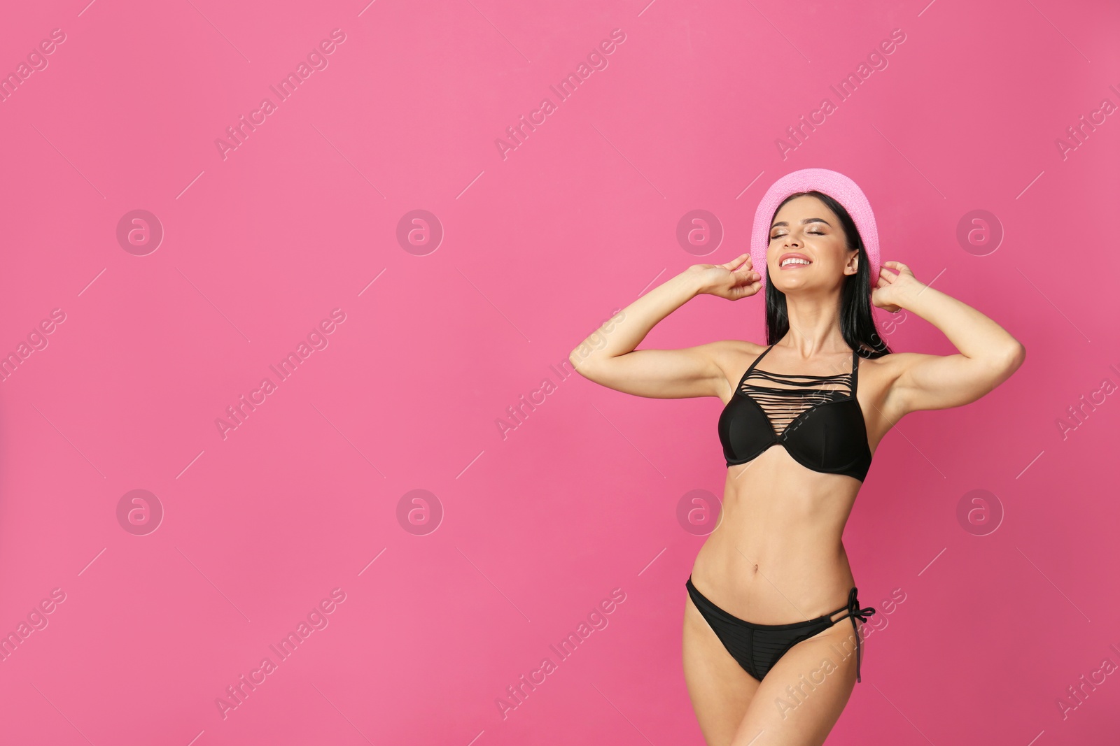 Photo of Beautiful young woman in black bikini with hat on pink background. Space for text