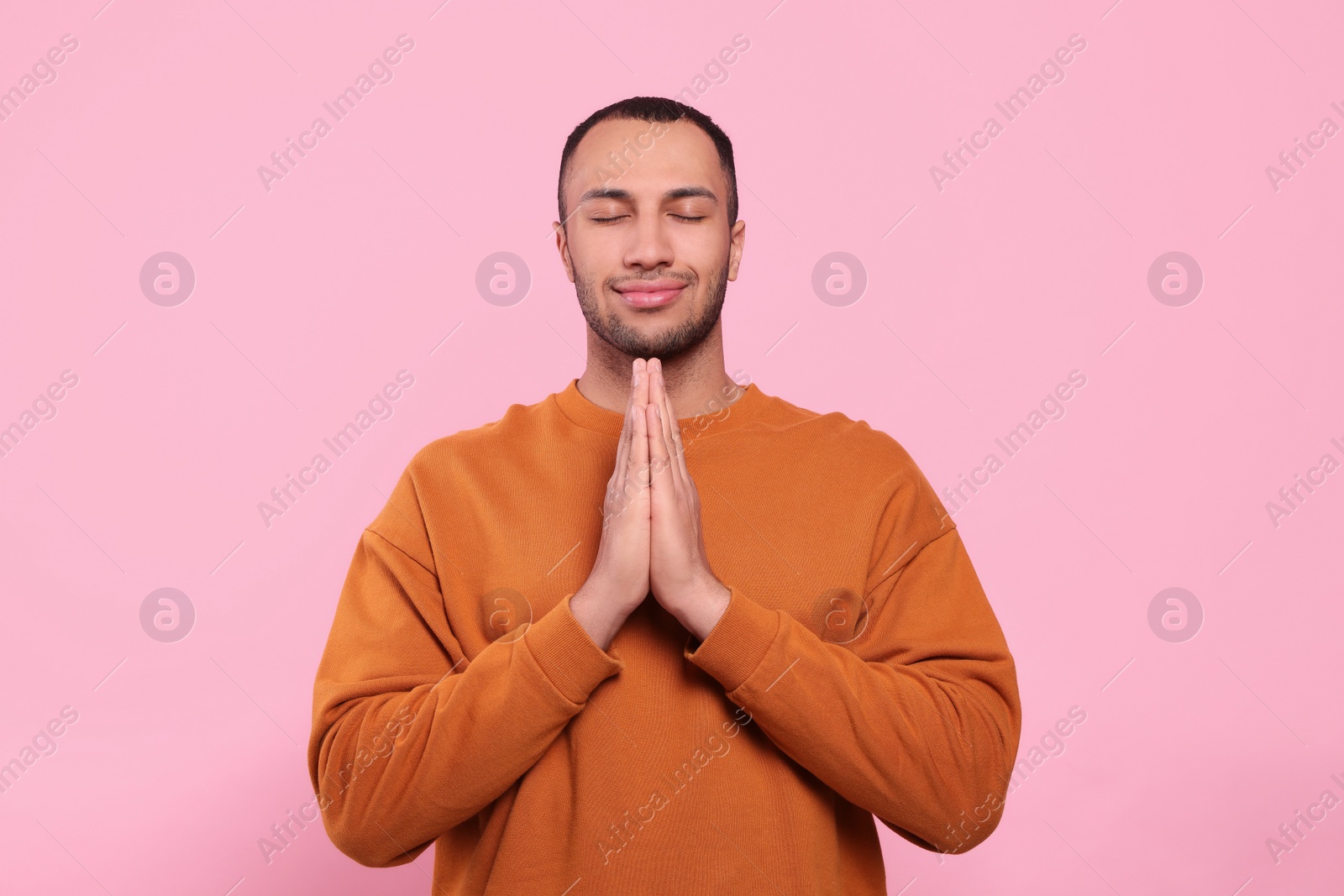 Photo of African American man with clasped hands praying to God on pink background