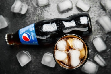 MYKOLAIV, UKRAINE - FEBRUARY 11, 2021: Glass of Pepsi, bottle and ice cubes on grey table, flat lay