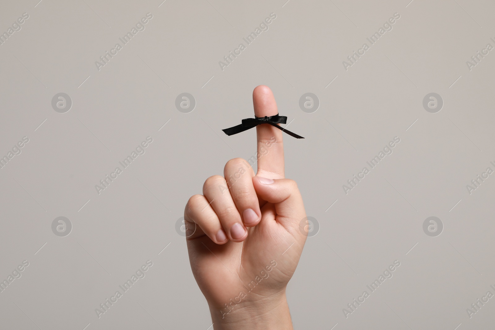 Photo of Man showing index finger with black tied bow as reminder on light grey background, closeup
