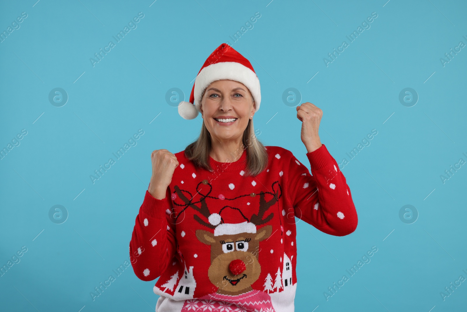 Photo of Happy senior woman in Christmas sweater and Santa hat on light blue background