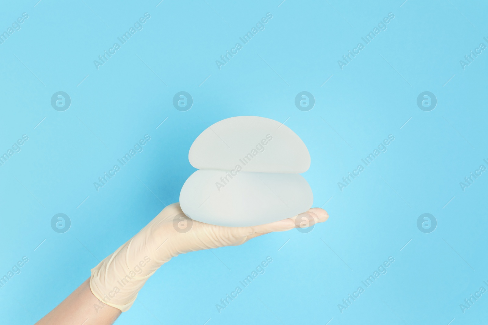 Photo of Doctor holding silicone implants for breast augmentation on color background, space for text. Cosmetic surgery