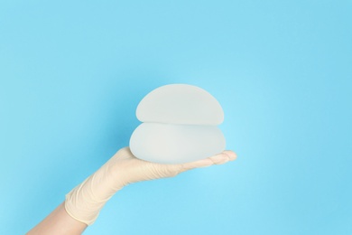 Doctor holding silicone implants for breast augmentation on color background, space for text. Cosmetic surgery