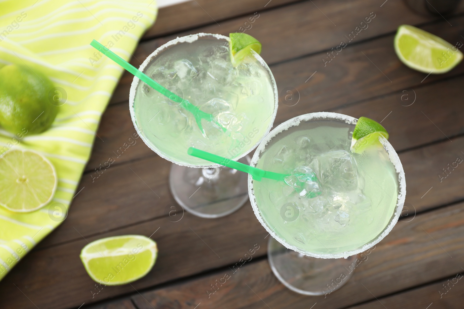 Photo of Delicious Margarita cocktail in glasses and lime on wooden table, above view