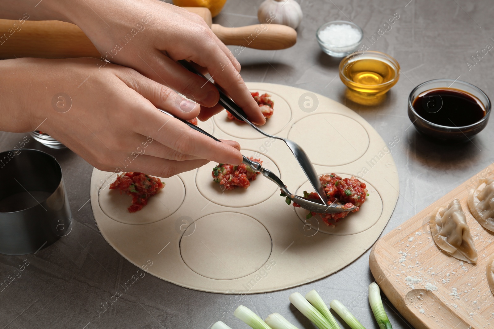 Photo of Woman cooking delicious gyoza at light grey table, closeup