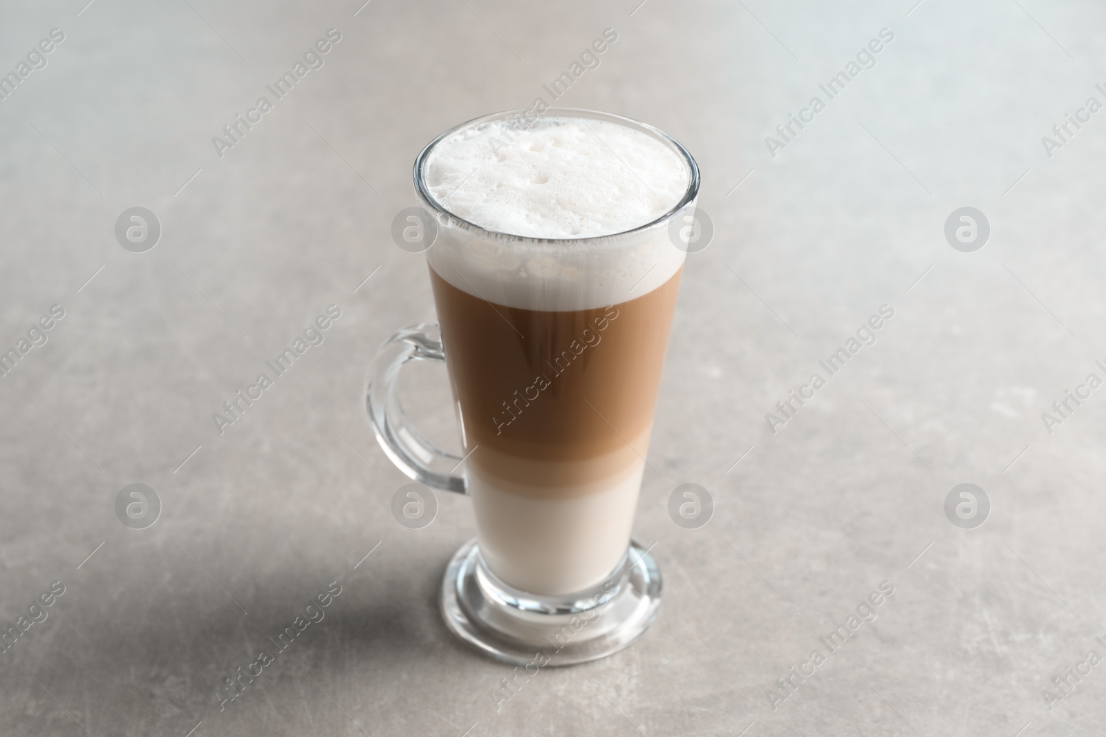 Photo of Glass cup of delicious layered coffee on light grey table