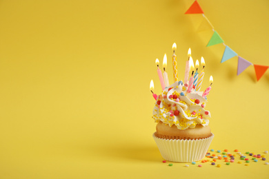 Photo of Birthday cupcake with candles on yellow background. Space for text