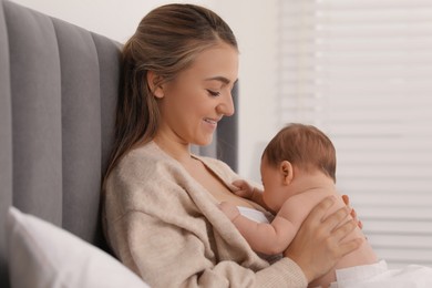 Mother holding her cute newborn baby on bed indoors