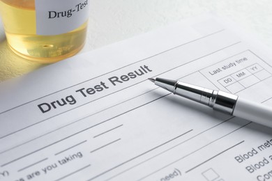 Photo of Drug test result form, container with urine sample and pen on light table, closeup