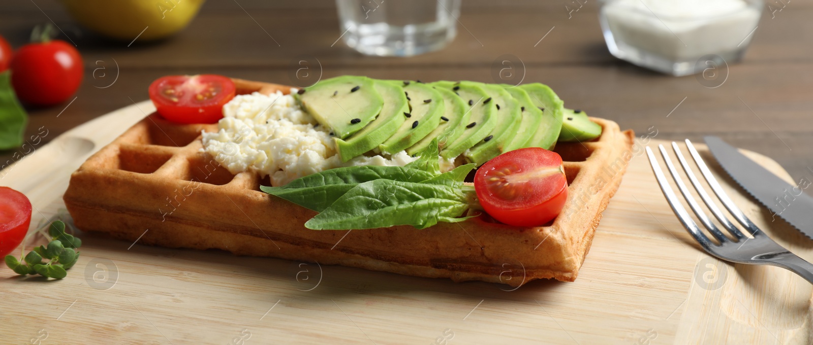 Photo of Fresh Belgian waffle with avocado, tomatoes and basil served for breakfast on wooden table