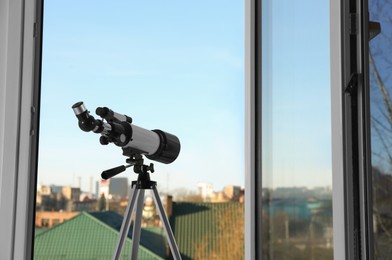 Photo of Tripod with modern telescope near open window indoors. Space for text