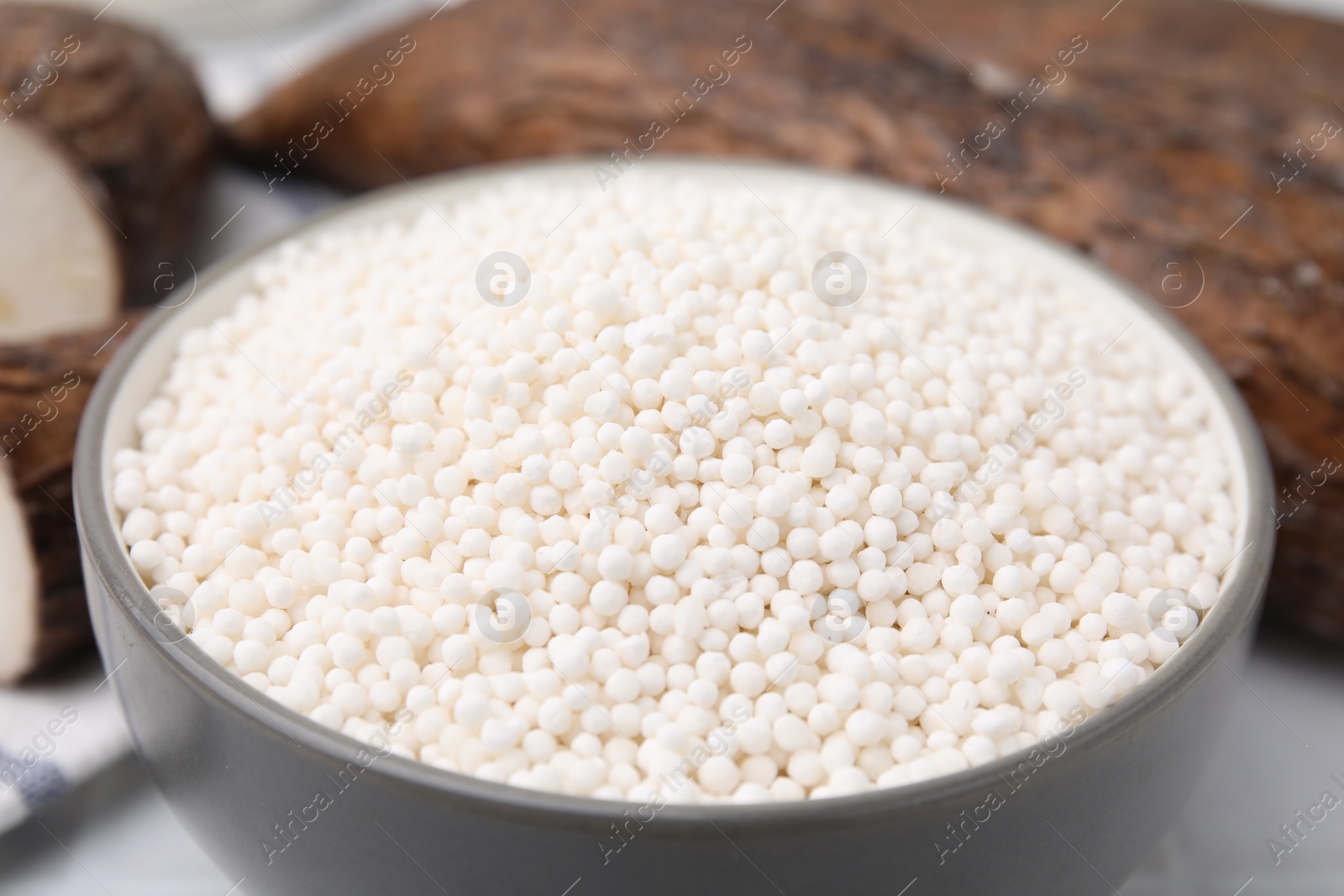 Photo of Tapioca pearls in bowl and cassava roots on table, closeup