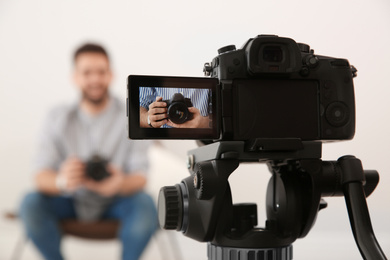 Photo of Young blogger with camera recording video indoors, focus on screen