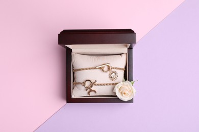 Photo of Beautiful jewelry and flower in box on color background, top view
