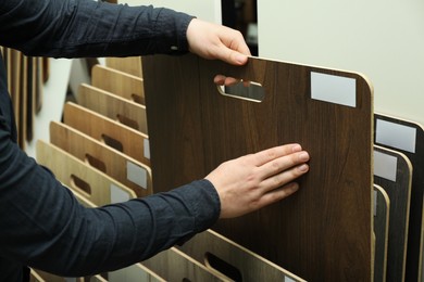 Photo of Man choosing wooden flooring among different samples in shop, closeup