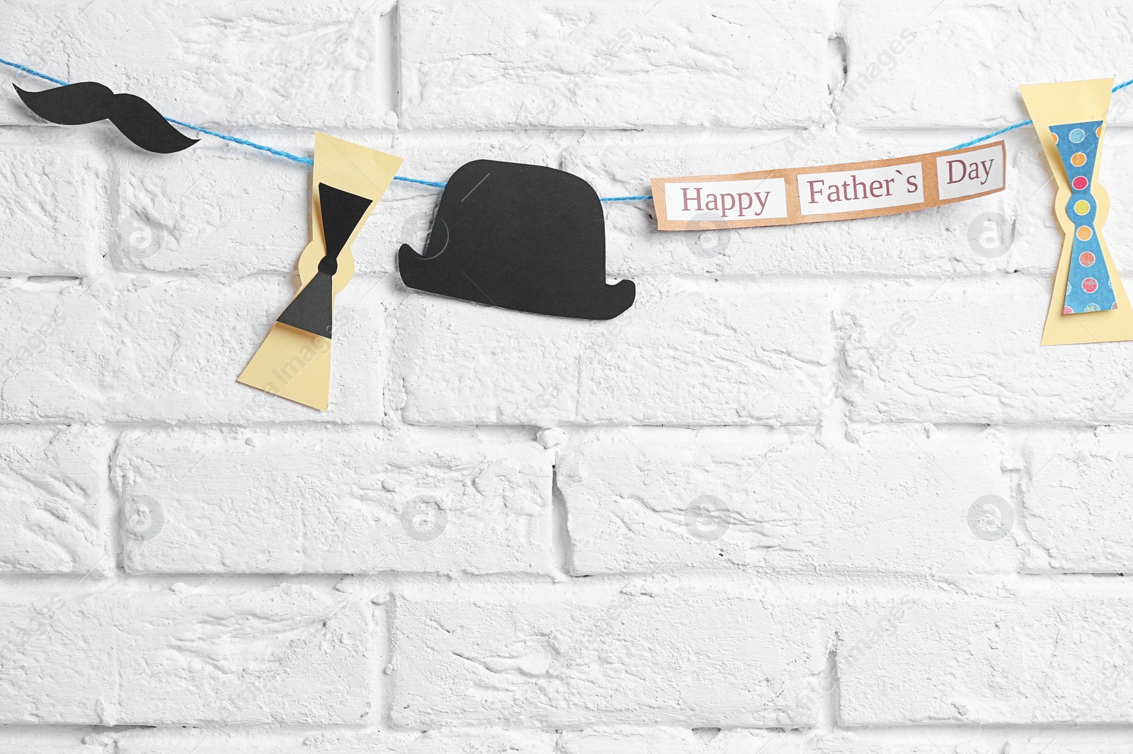 Photo of Bow ties, hat and mustache hanging on rope against brick wall background