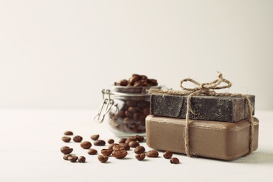 Photo of Handmade soap bars and coffee beans on white table. Space for text