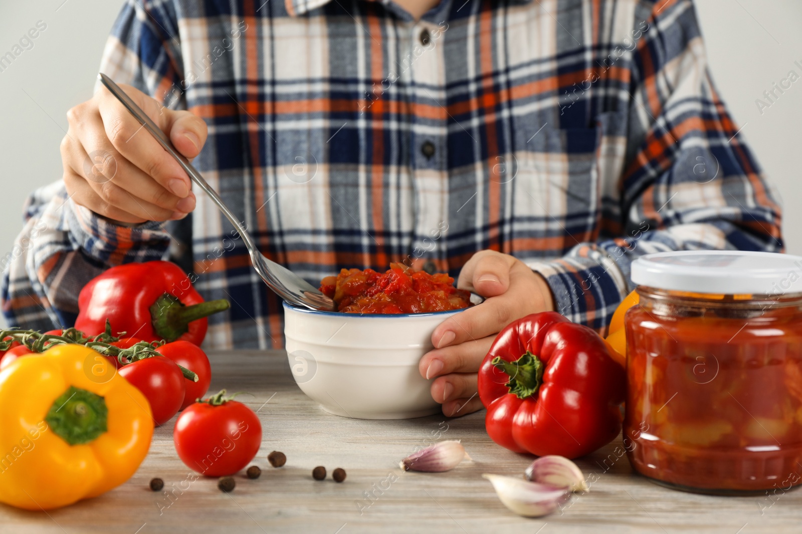 Photo of Woman eating tasty lecho at wooden table, closeup