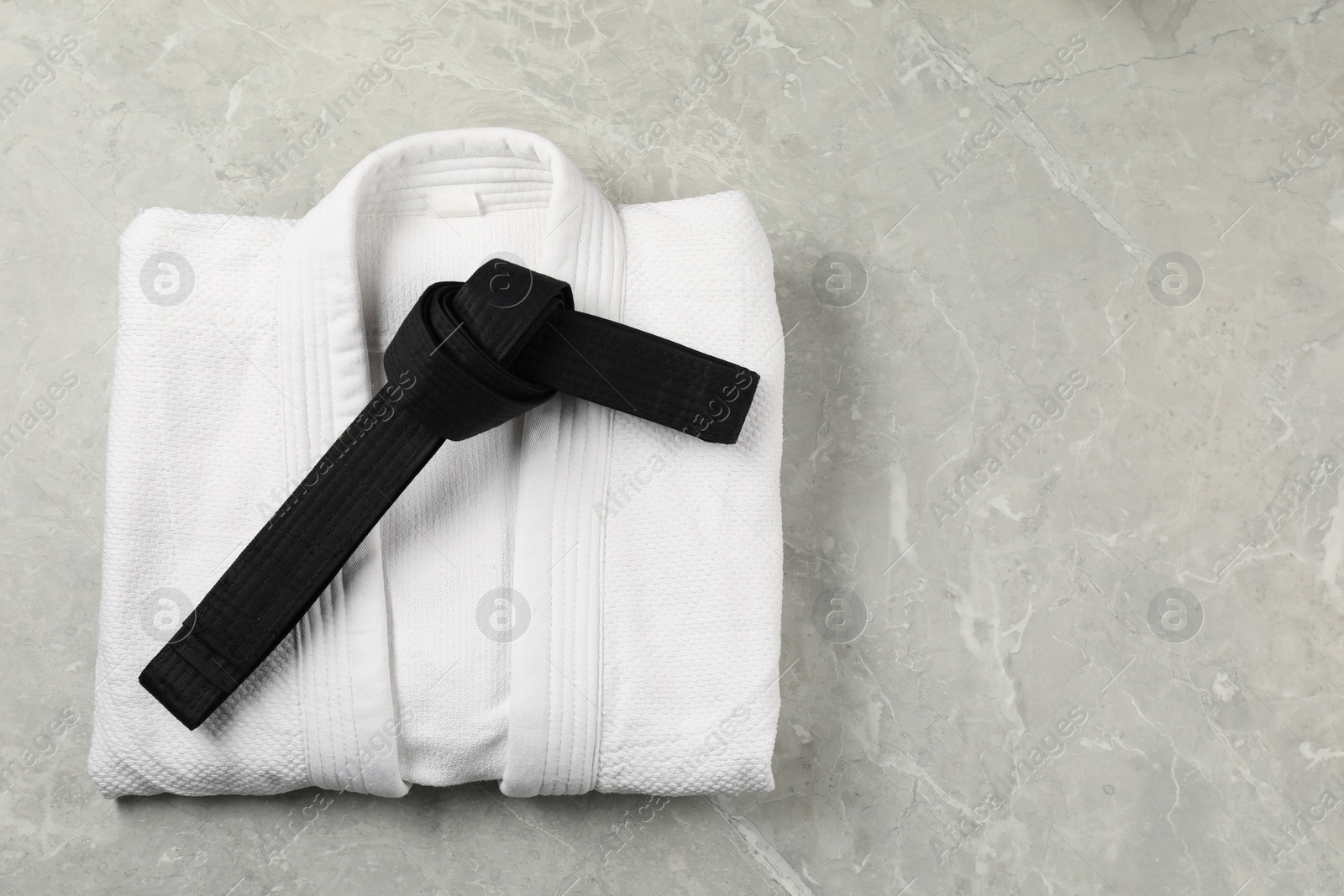 Photo of Black karate belt and white kimono on gray marble background, top view. Space for text