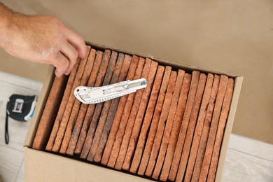 Photo of Worker near box with many decorative bricks and utility knife indoors, closeup