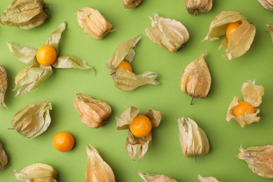 Photo of Ripe physalis fruits with calyxes on light green table, flat lay