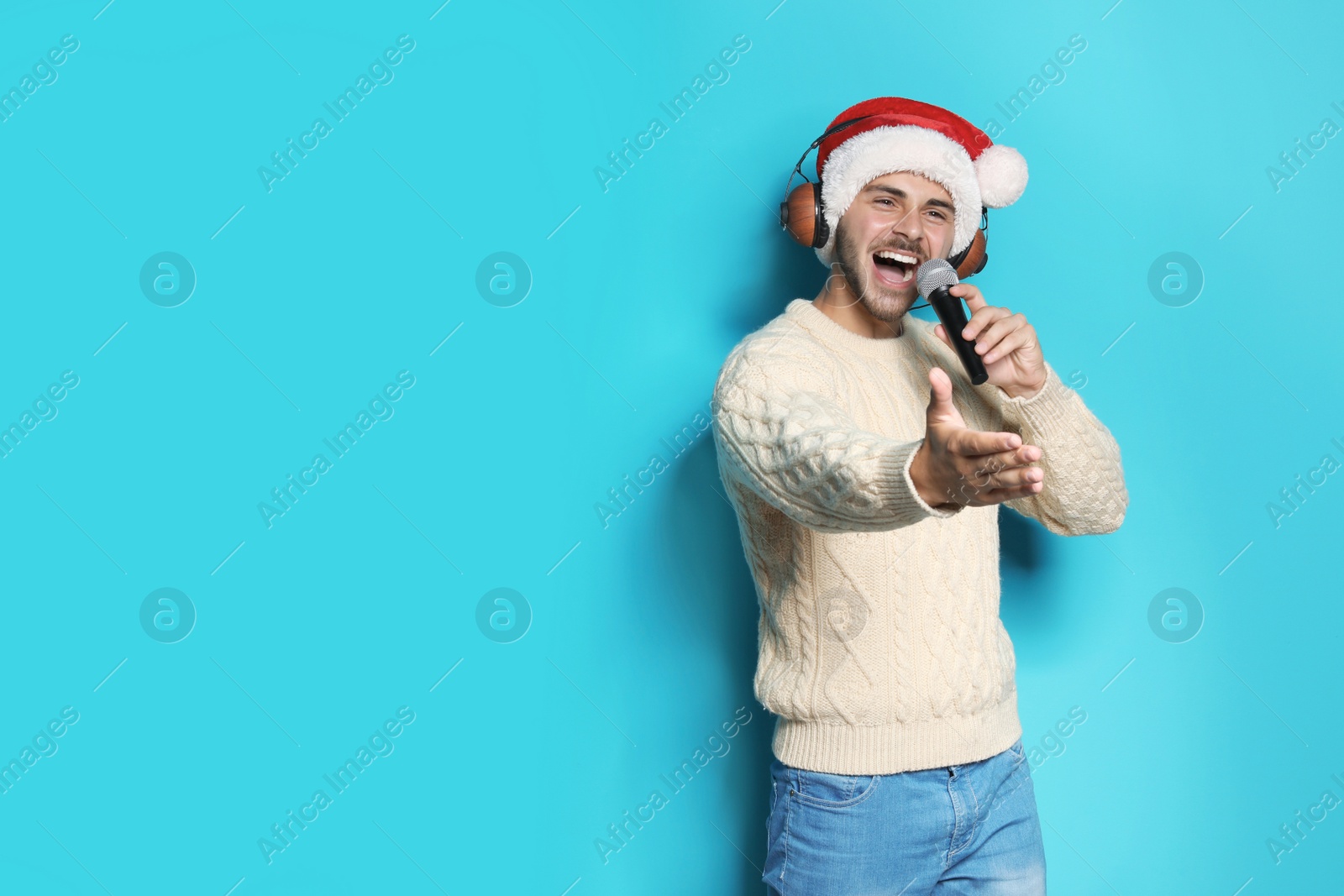 Photo of Young man in Santa hat singing into microphone on color background. Christmas music