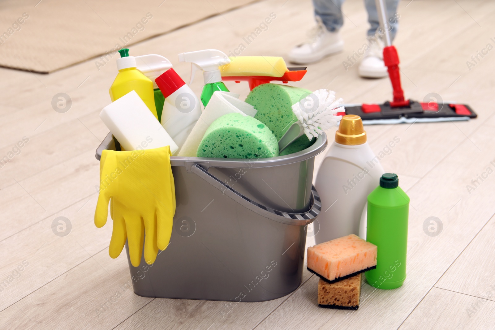 Photo of Different cleaning supplies in bucket and woman mopping floor, selective focus