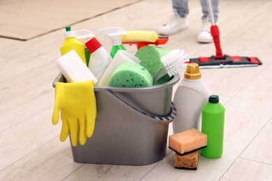 Photo of Different cleaning supplies in bucket and woman mopping floor, selective focus