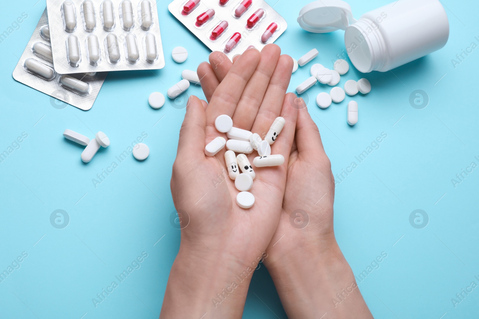 Photo of Woman holding antidepressants with different emoticons on light blue background, top view