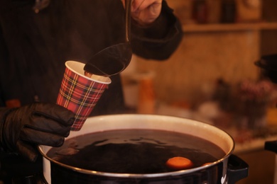 Seller pouring hot mulled wine into cup at fair, closeup. Space for text