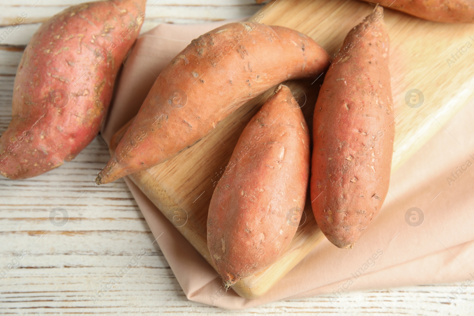 Photo of Board with sweet potatoes on white wooden background