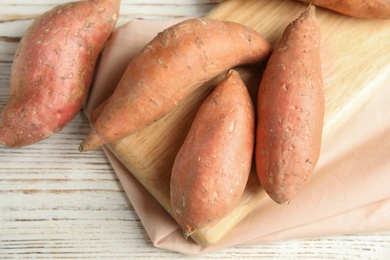 Photo of Board with sweet potatoes on white wooden background