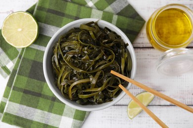 Photo of Tasty seaweed salad in bowl served on wooden table, flat lay