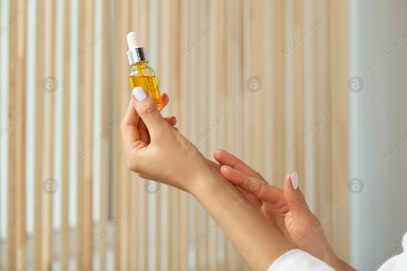 Photo of Young woman with bottle of essential oil indoors, closeup