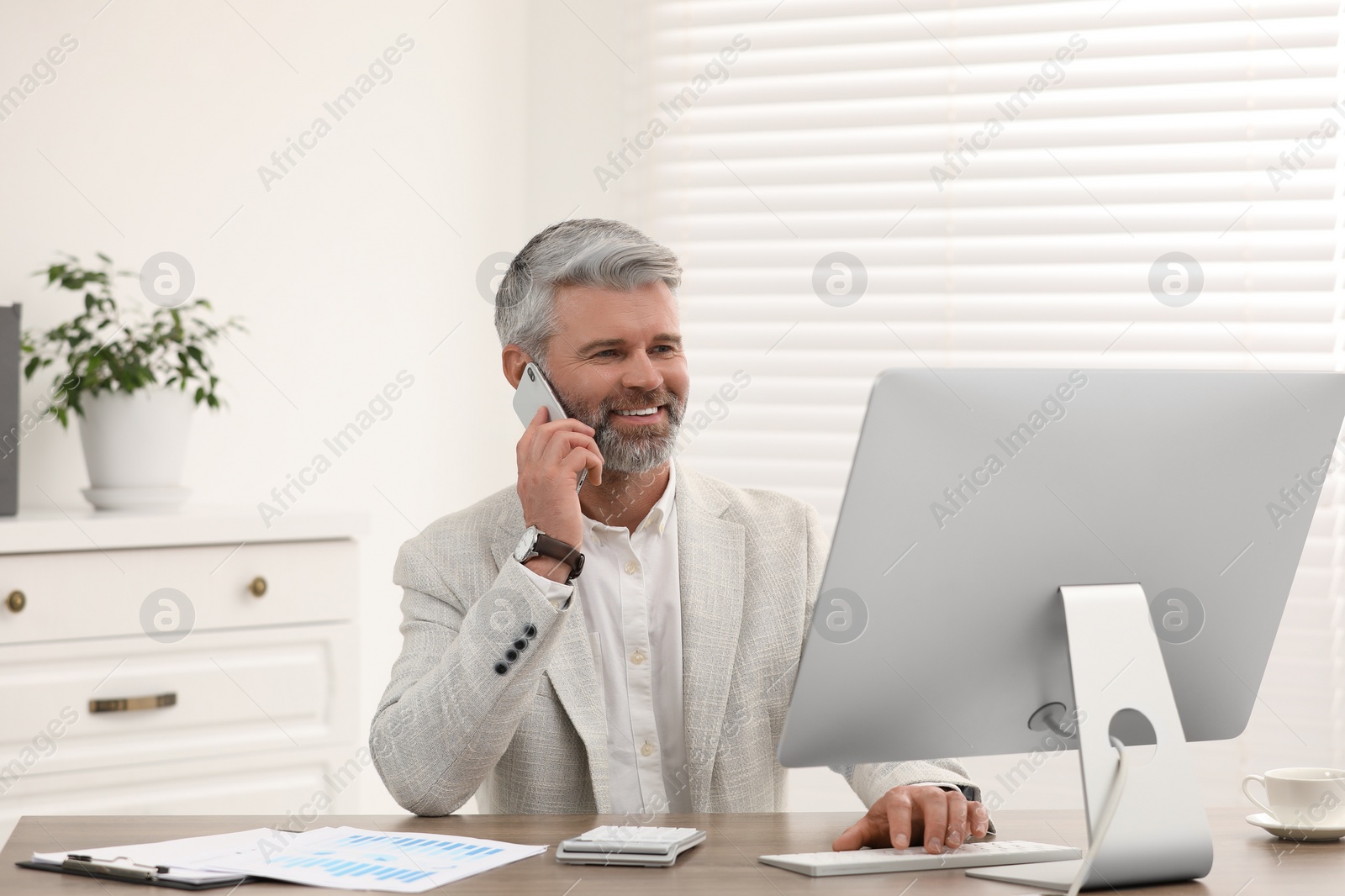 Photo of Professional accountant talking on phone and working at wooden desk in office