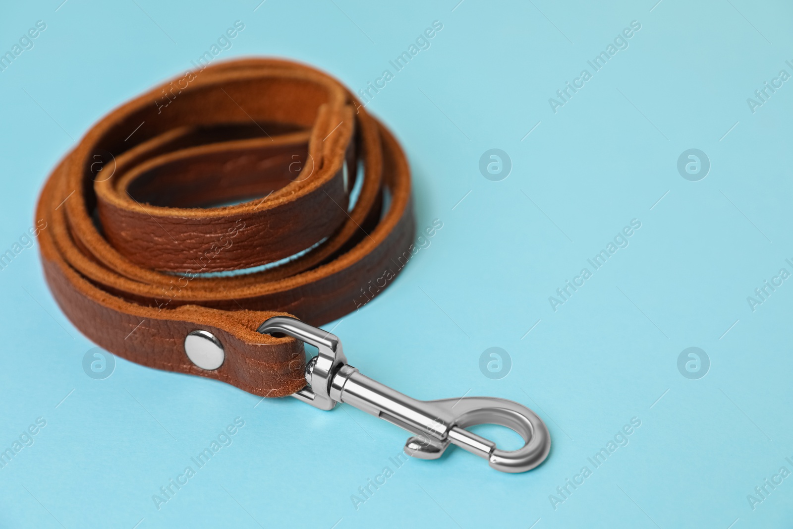 Photo of Brown leather dog leash on light blue background, closeup. Space for text