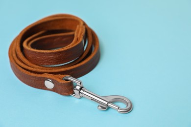 Photo of Brown leather dog leash on light blue background, closeup. Space for text