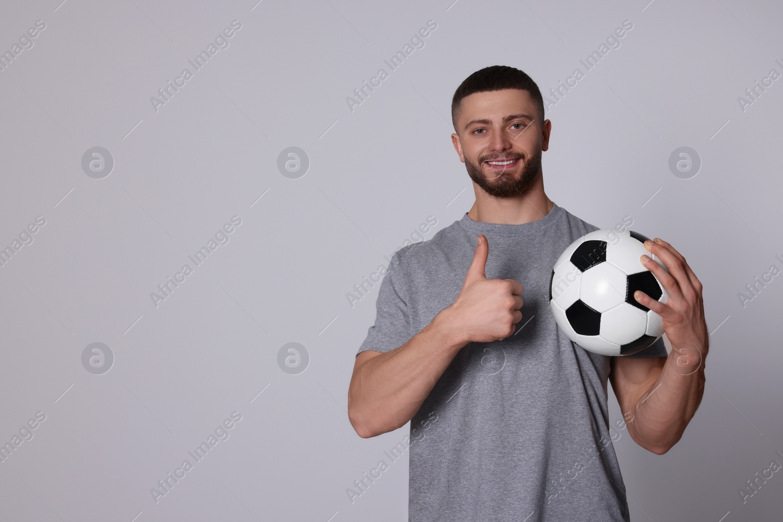 Photo of Athletic young man with soccer ball showing thumb up on light grey background. Space for text