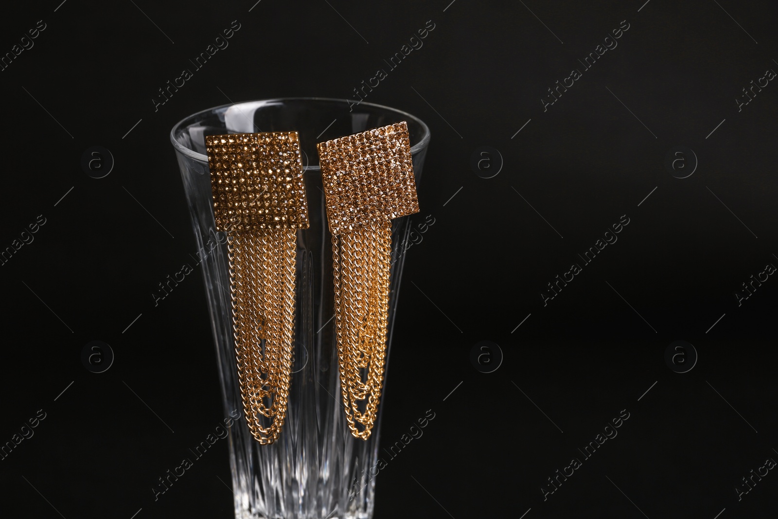 Photo of Elegant earrings on glass against black background, space for text. Luxury jewelry