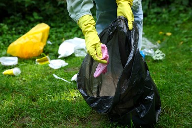 Woman with plastic bag collecting garbage on green grass outdoors, closeup