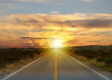 Image of Empty asphalt road through field at sunset