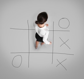 Image of Young woman and illustration of tic-tac-toe game on grey background, above view. Business strategy concept 