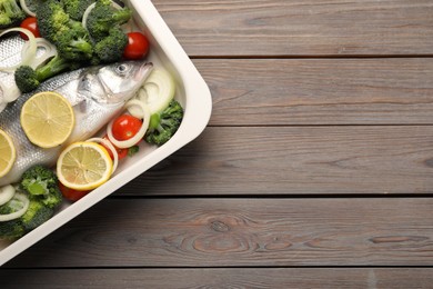 Photo of Raw fish with vegetables and lemon in baking dish on wooden table, top view. Space for text