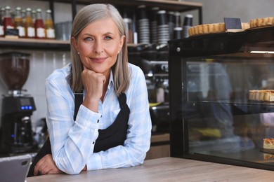 Photo of Portrait of smiling business owner at cashier desk in her cafe