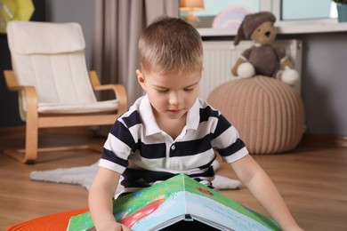 Cute little boy reading book on floor at home